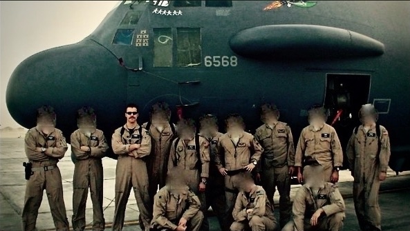 A group of uniformed individuals poses in front of a large military aircraft on a tarmac.